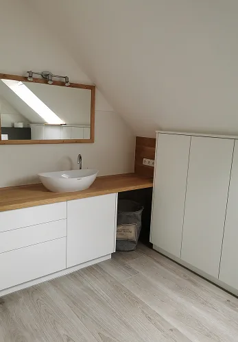 Modernes Badezimmer mit weißem Waschbecken, Holzarbeitsplatte, großem Spiegel und weißem Schrank.