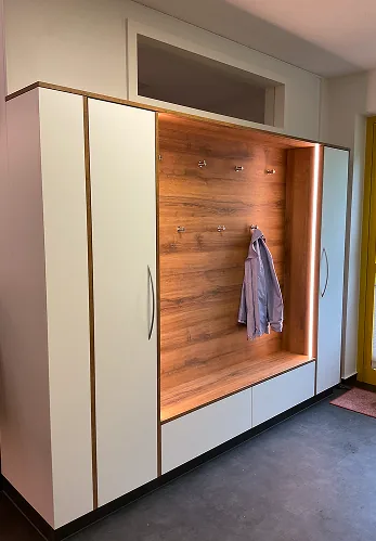 Weiße Garderobe mit Holzrückwand, drei Haken und einer Jacke im Flur neben gelbem Fenster.